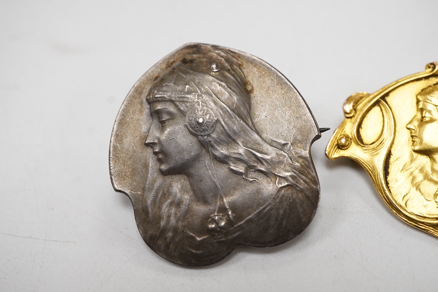 Two Art Nouveau medallion brooches, yellow metal embossed with the bust of a lady to dexter, lacking pin and a similar 900 standard white metal brooch, 28mm.
